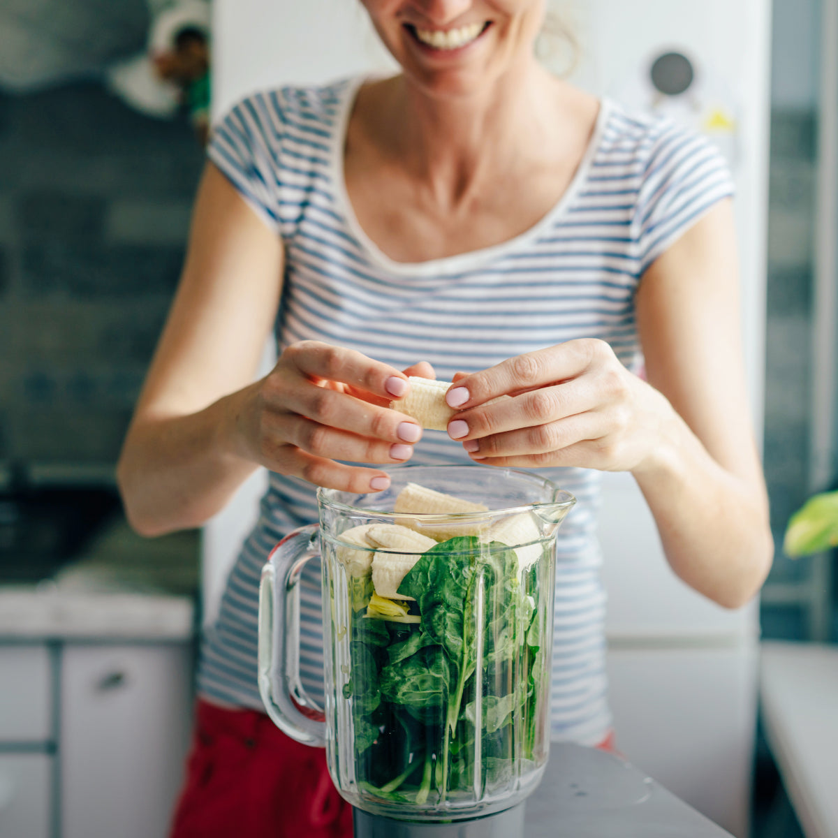 woman making smoothie with banana and greens